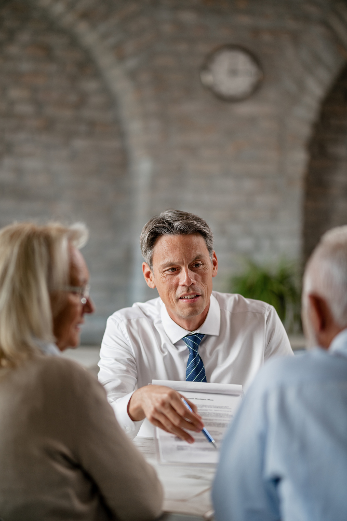 Smiling bank manager showing to his senior customers where to sign on the contract during a meeting in the office.