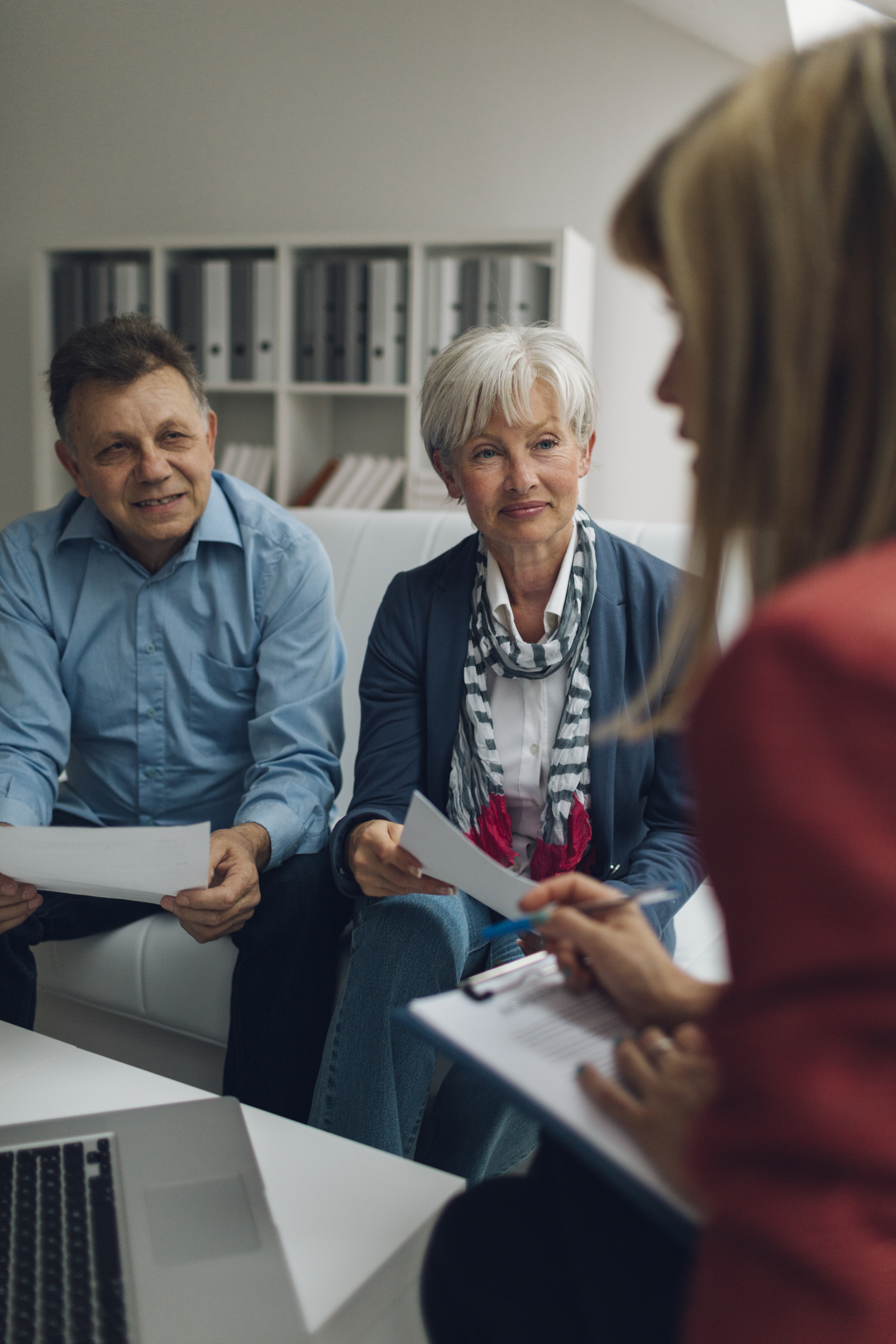 Mature Couple Meeting with Financial Advisor, selective focus to senior man and mature woman listening to financial advisor. She is holding contract and explaining about retirement and insurance options for them.